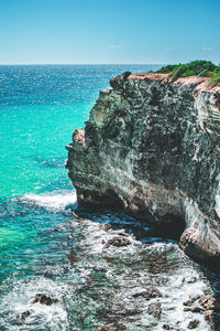 Rock formation in sea against clear blue sky