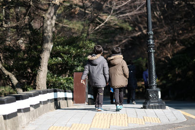 Rear view of siblings walking on footpath against trees