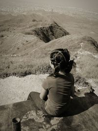 Girl sitting on retaining wall against landscape