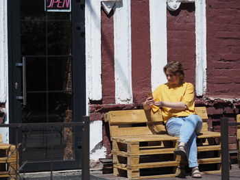 A woman of european appearance sits with a telephone in the summer on an old wooden bench against 