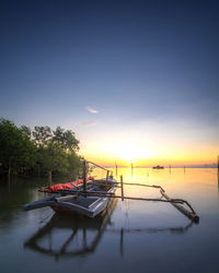 Boat moored in sea against sky during sunset