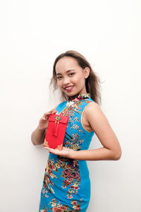 Portrait of smiling young woman holding envelope while standing against white background