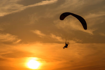 Silhouette person paragliding against sky during sunset