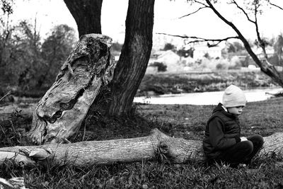 Man sitting by tree trunk on field