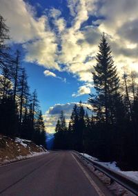 Empty road amidst bare trees against cloudy sky