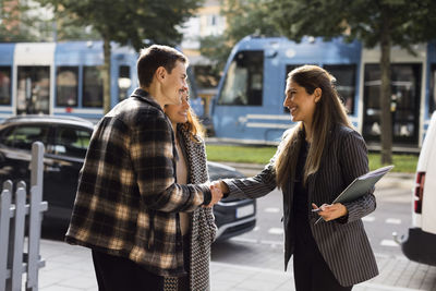 Smiling man doing handshake with female real estate agent while standing at street