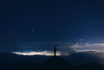 Silhouette man standing on mountain peak against sky at night