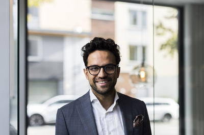 Portrait of smiling male real estate against glass door in office