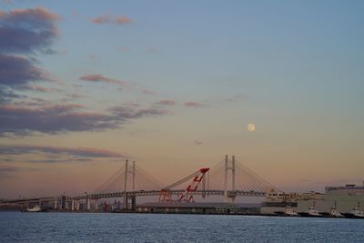 Suspension bridge over sea against sky during sunset