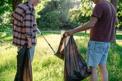 Volunteers collect a discarded plastic bottle from grass into a black trash bag.