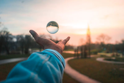 Close-up of hand holding crystal ball against trees