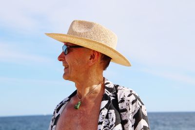 Smiling senior man looking at sea while wearing hat against sky