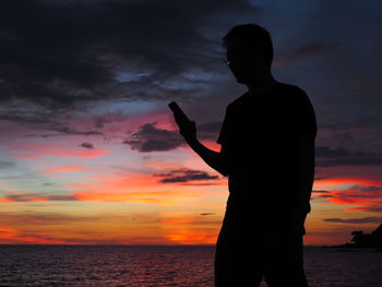 Silhouette man using smart phone against sky during sunset