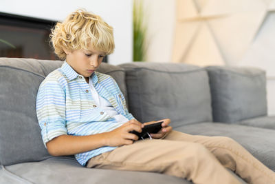 Boy using mobile phone while sitting on sofa
