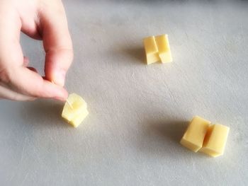Cropped hand of person holding toothpick on pineapple cube by cheese on table