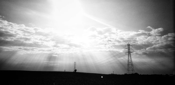 Silhouette electricity pylon on field against sky