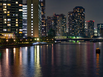 Illuminated buildings by river against sky at night