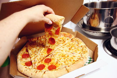 Cropped image of person holding pizza slice from box