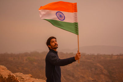Man holding indian flag on mountain against sky