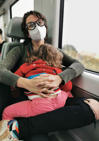 View of mother with daughter on her lap traveling by train.