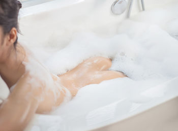 Rear view of naked young woman taking bath in bathtub