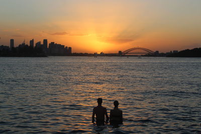 Silhouette men in sea against sky during sunset