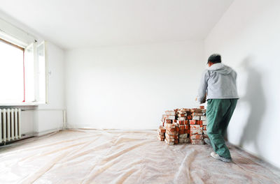 Rear view of man arranging bricks by wall at home during renovation