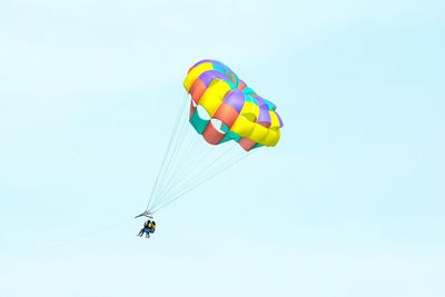 Low angle view of people parasailing against clear sky