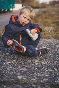 Full length portrait of cute boy holding his foot while sitting on road