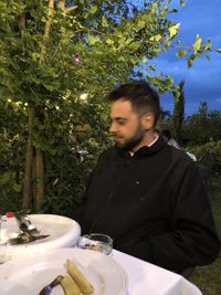 Young man looking away while sitting on tree