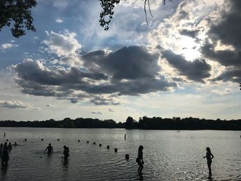 People swimming in lake against sky during sunset