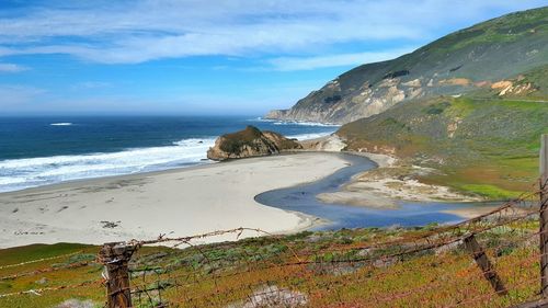 Scenic view of beach by hill against sky