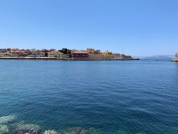 Scenic view of sea by buildings against clear blue sky