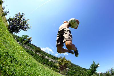 Low angle view of boy jumping against blue sky