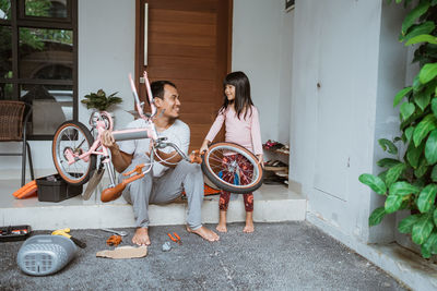 Smiling father repairing bicycle with daughter at home