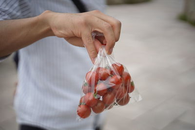 Midsection of man holding cherry tomatoes in plastic bag