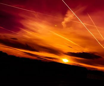 Scenic view of silhouette vapor trails in sky during sunset