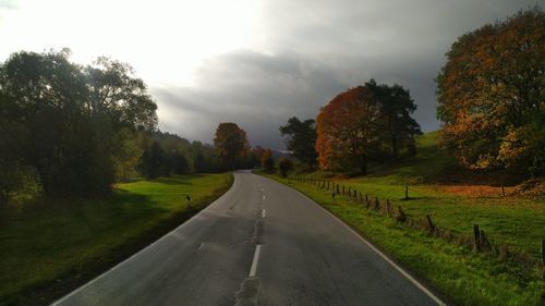 Empty road along trees and plants against sky