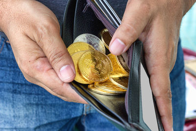 Midsection of man holding bitcoins in wallet