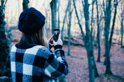 Rear view of woman photographing through mobile phone in forest