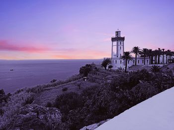 Lighthouse by sea against sky during sunset