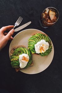 Cropped hand by breakfast in plate on table