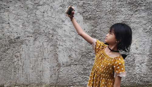 Young woman drinking water while standing against wall
