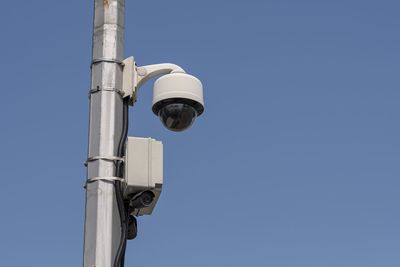 Low angle view of security camera against clear blue sky during sunny day