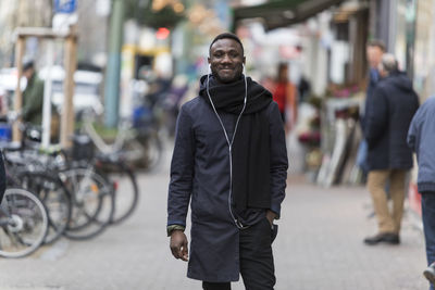 Portrait of smiling man listening music while standing on footpath in city