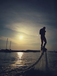 Man flyboarding in sea against sky during sunset