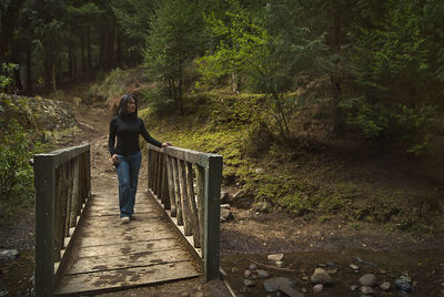 Woman walking on footbridge in forest