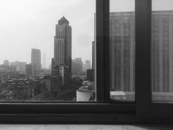 Buildings in city against sky seen through glass window