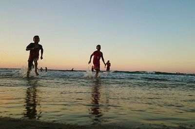 Men playing on beach against sky during sunset