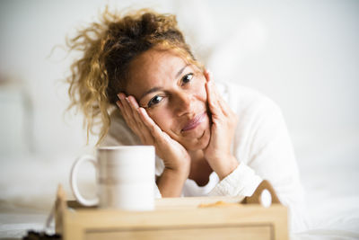 Portrait of woman with coffee cup on bed at home